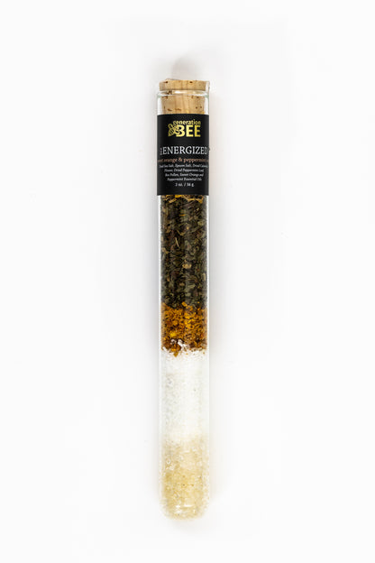 A glass vial of Energized soaking salts with layers of dried herbs, bee pollen, and bath salts.