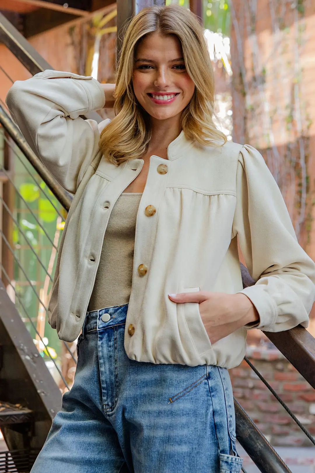 Woman wearing a cream Bette Suede Blouson Hem Button Up Jacket with a stand collar and side pockets.