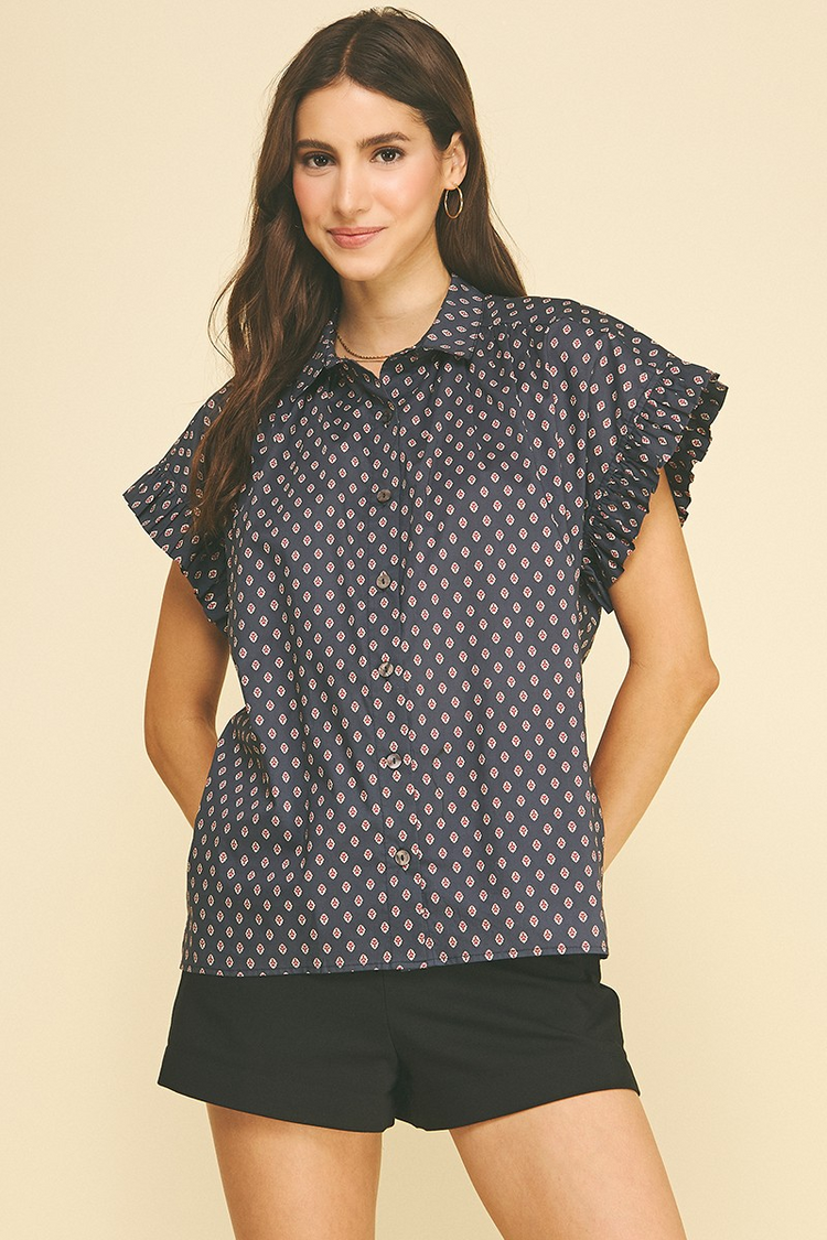 Woman wearing the Emiliana Geometric Diamond Print Shirt with ruffled cap sleeves and black shorts.