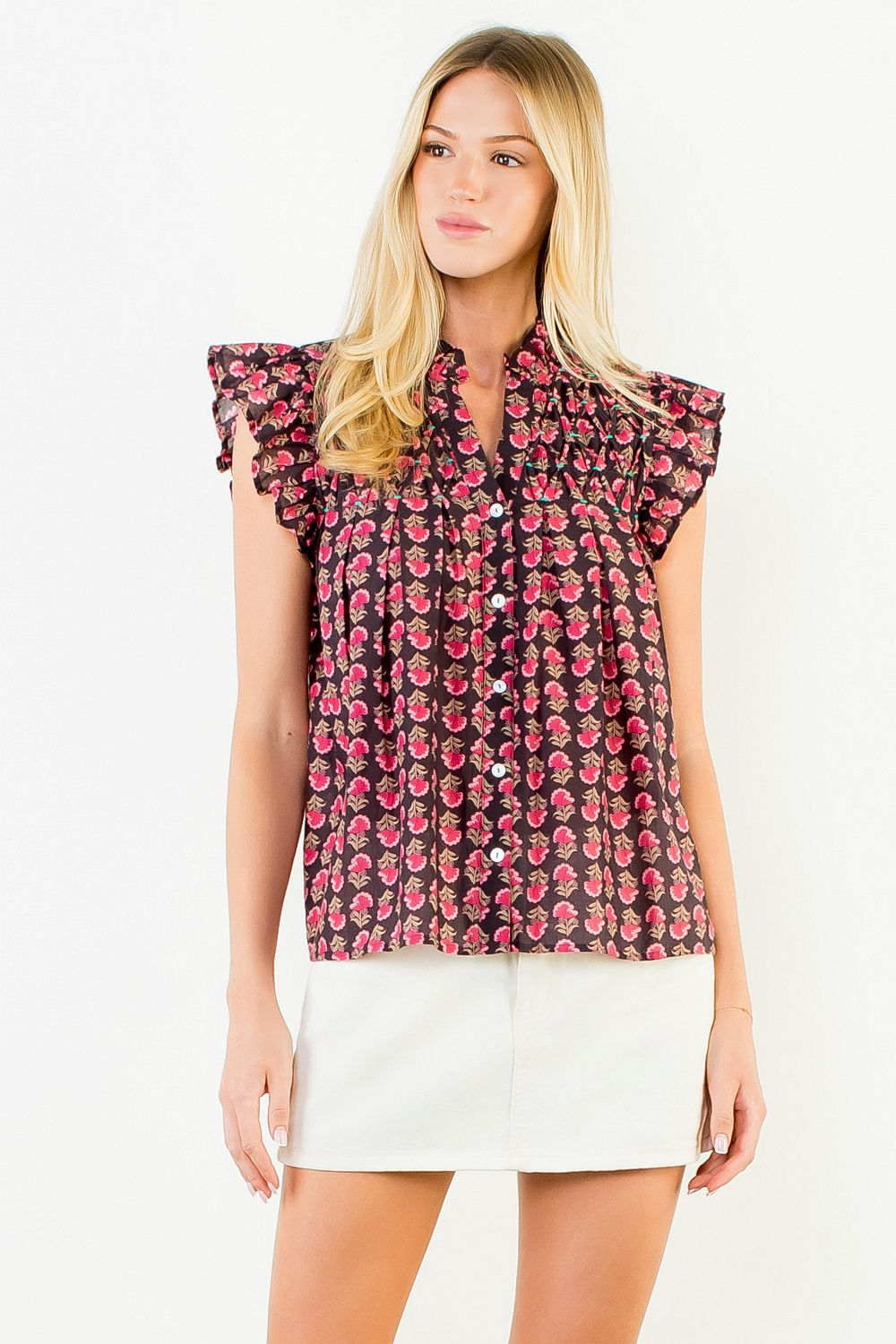 Woman wearing a Jane Flutter Sleeve Button Top in a dark floral print with a white mini skirt.