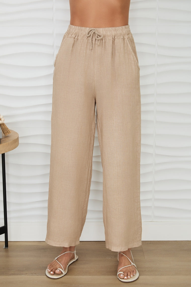 Woman wearing Hannah linen drawstring mid-rise pants in beige with side pockets and white sandals.
