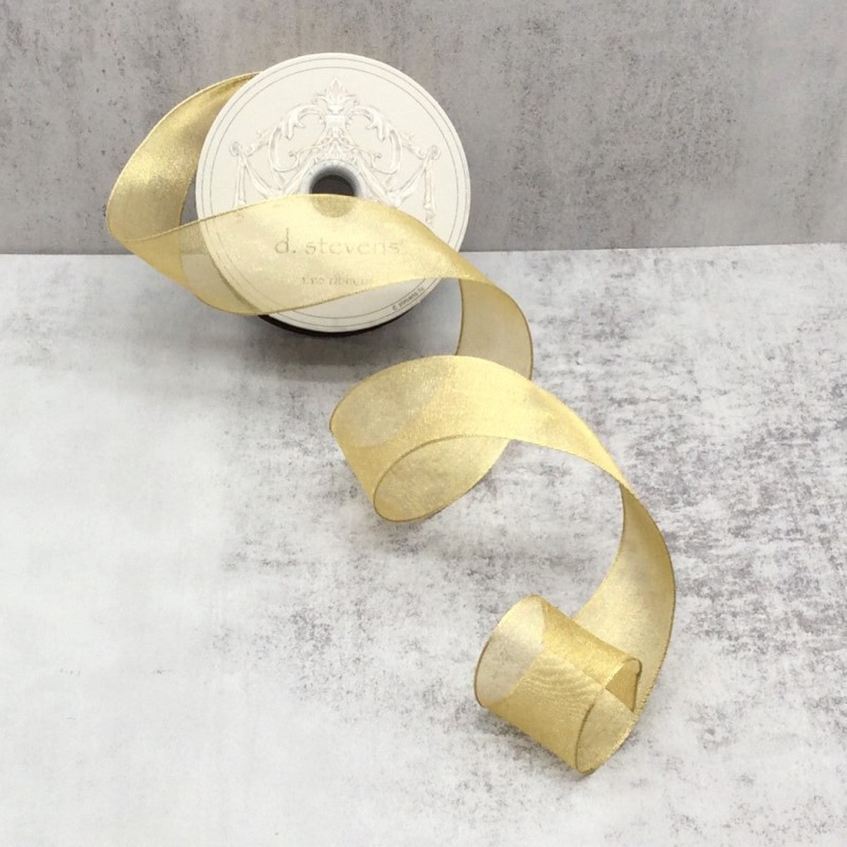 1.5 inch wide gold metallic mesh ribbon unspooled on a grey textured surface.