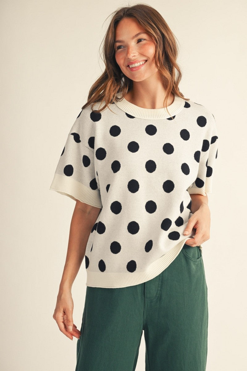 Woman wearing the Emily Polka Dot Comry Sweater Top in white with black dots and green pants.