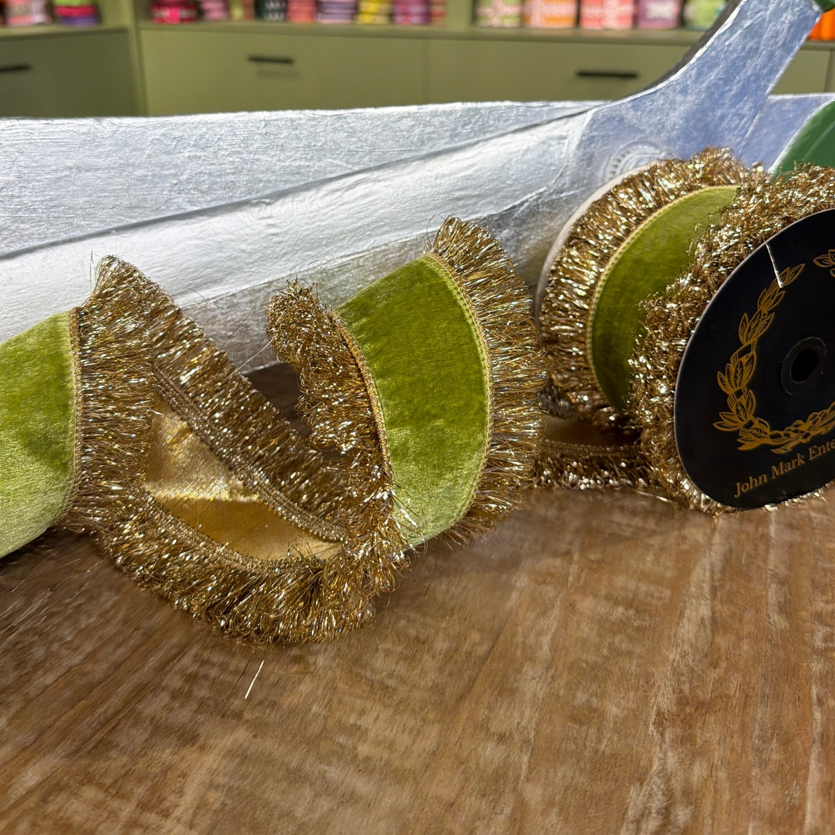 Apple green velvet ribbon with double-sided metallic gold fringe trim on a wooden surface.