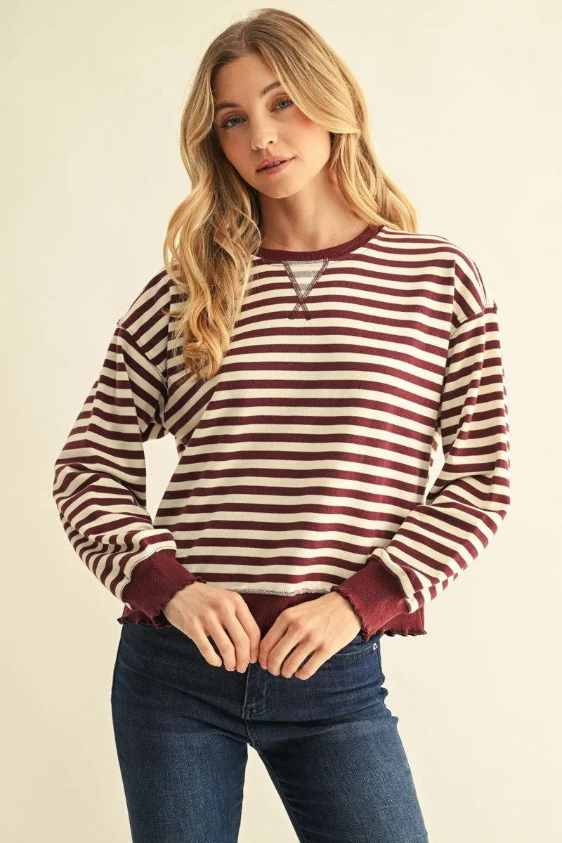 Woman wearing a burgundy and cream striped long-sleeve French terry sweatshirt with blue jeans.