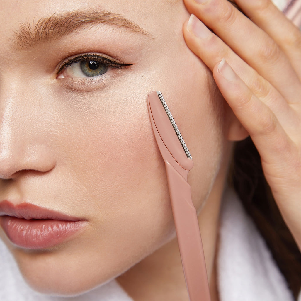 Blush-colored eco-friendly dermaplaner tool with ergonomic handle