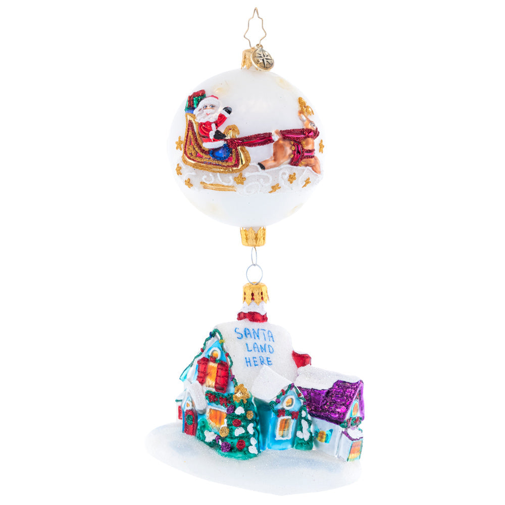 Glass Christmas ornament with Santa in a sleigh on a globe above a snowy Santa Land house.