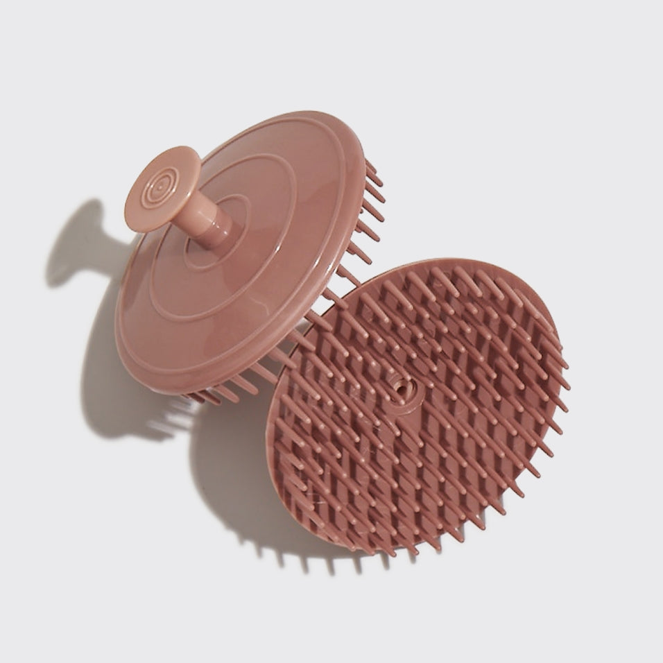 Scalp exfoliator with soft flexible bristles in a compact black handle made from recycled materials.
