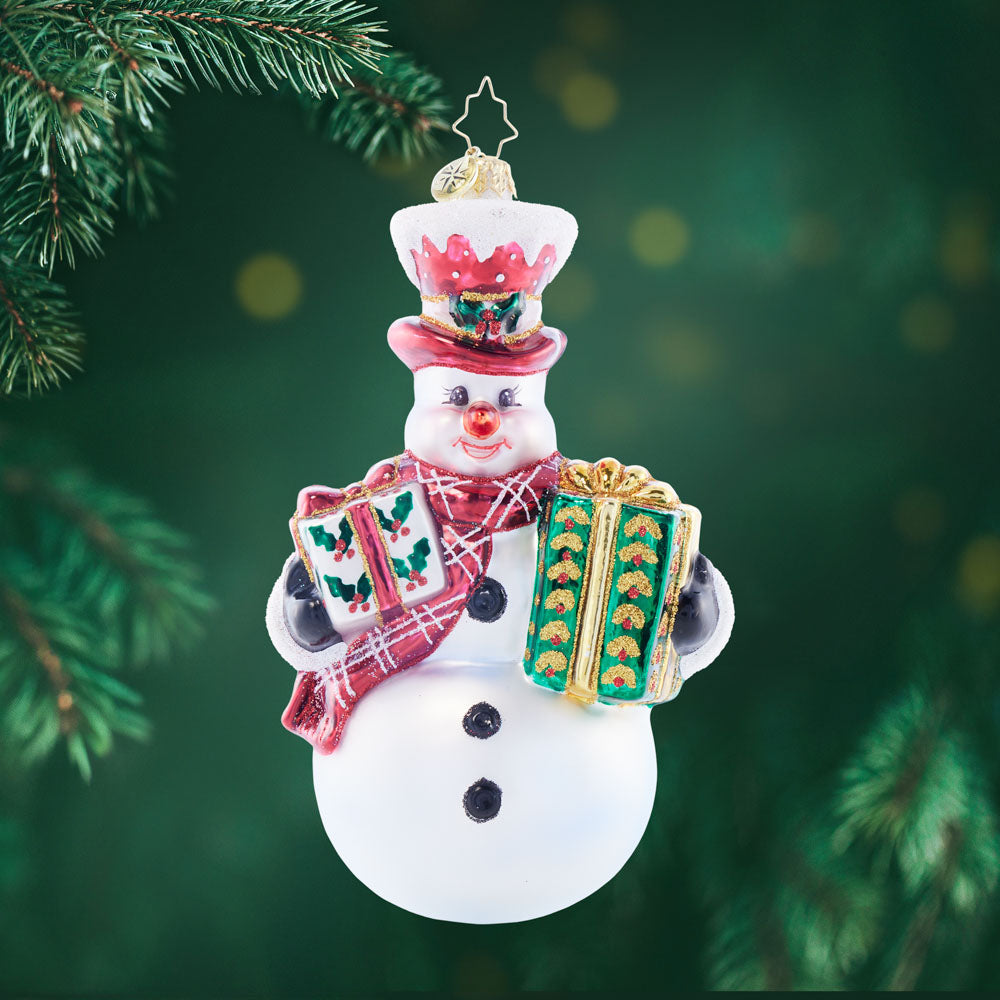 Snowman Christmas ornament wearing a red top hat and scarf, holding two wrapped gifts.