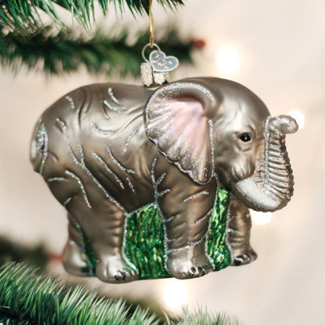 Large glass elephant Christmas ornament with silver glitter accents hanging on a tree branch.