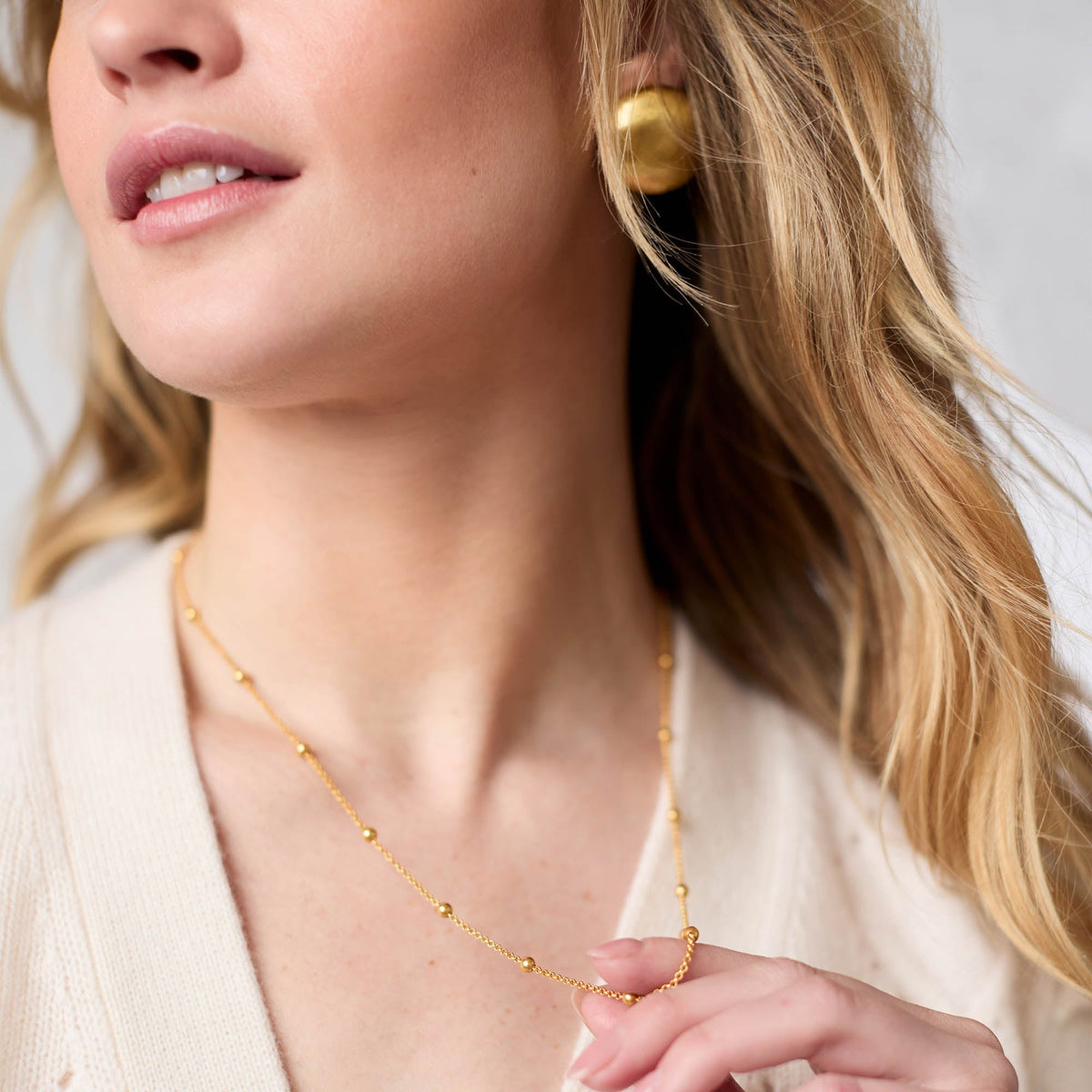 A woman wearing the Solara Delicate Station Necklace, a thin gold chain with small bead accents.