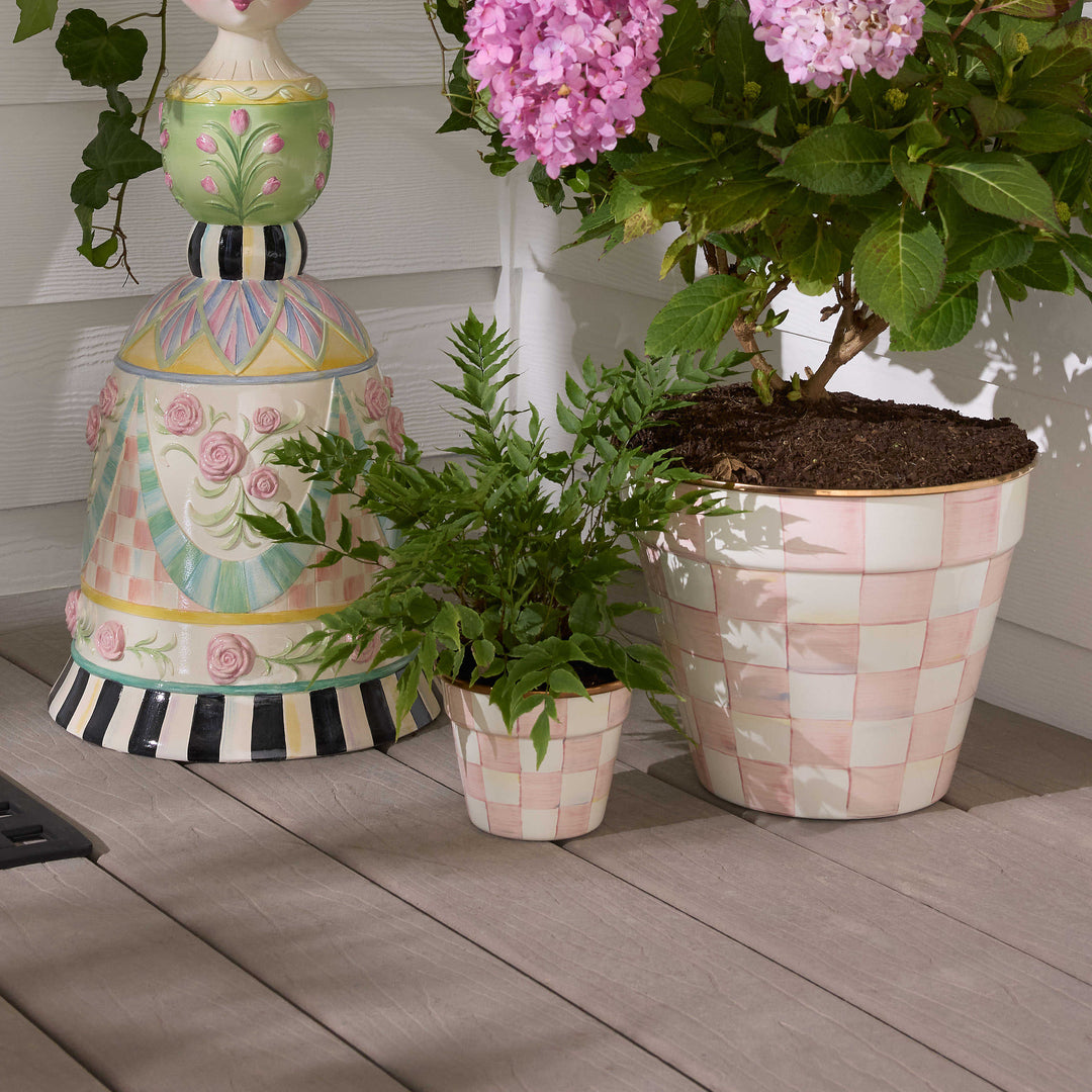Small hand-painted pink and white checkered garden pot with a green fern on a wooden deck.