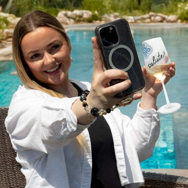 Woman wearing a black crystal beaded wristlet phone strap with a gold clasp by a pool.