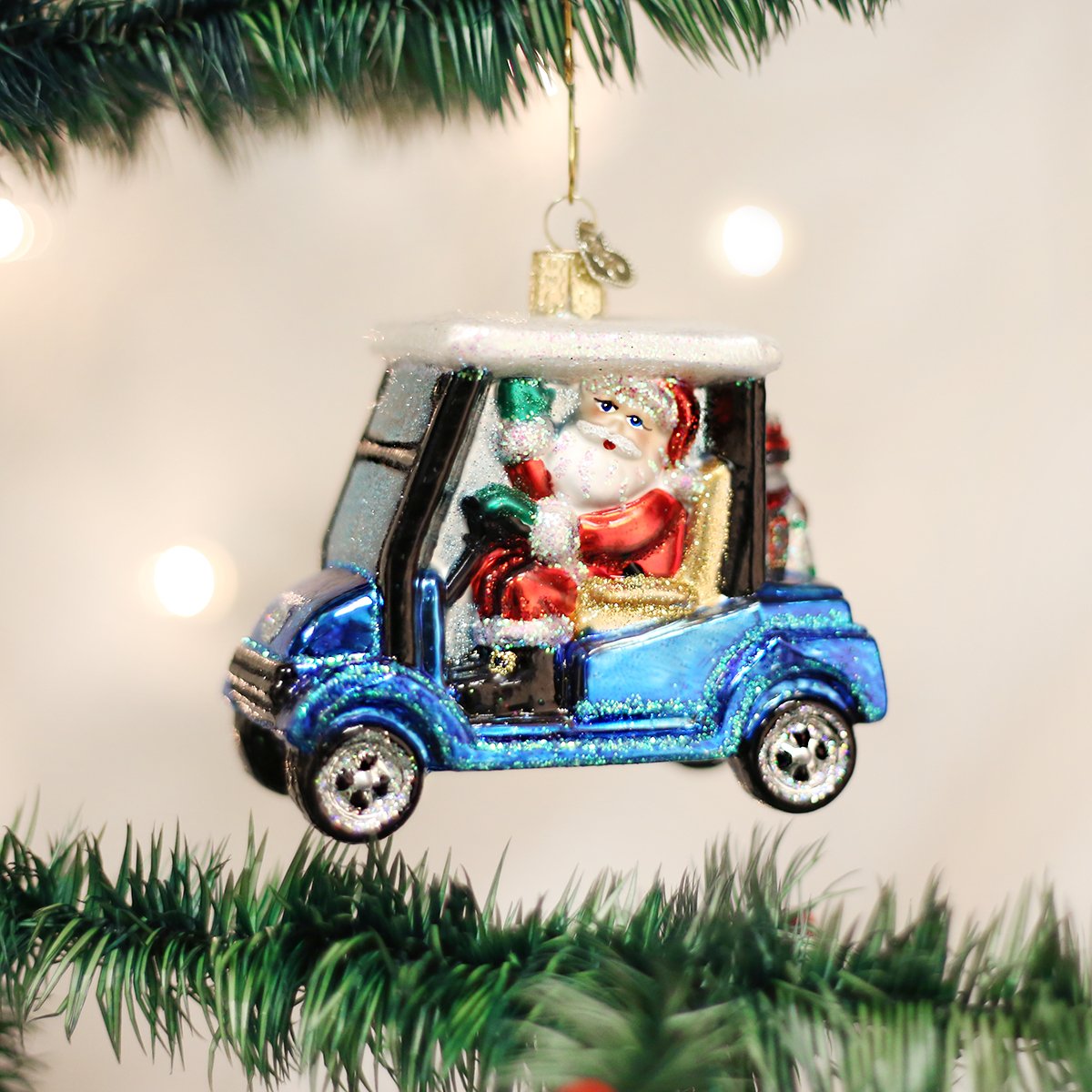 Glass Christmas ornament of Santa Claus driving a blue glittery golf cart on a tree.