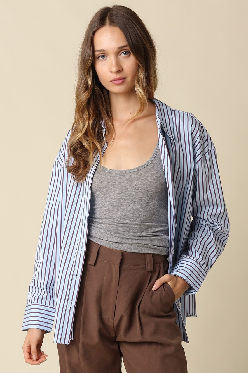 Woman wearing a blue and brown Clover Stripe Oversized Shirt over a grey tank and brown trousers.