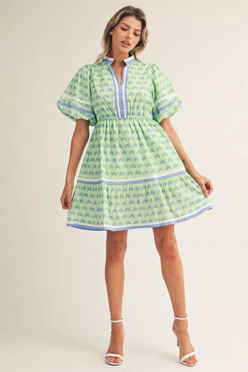 Woman in a green and blue floral print mini dress with puff sleeves and a tiered skirt.