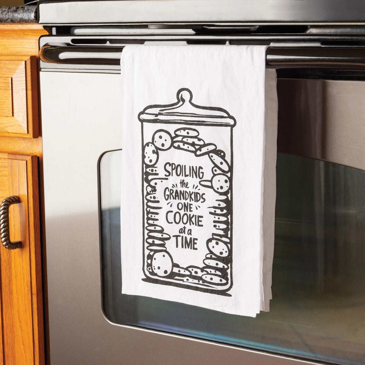 White cotton kitchen towel with a black graphic of a cookie jar filled with cookies and the text "Spoiling the grandkids one cookie at a time."