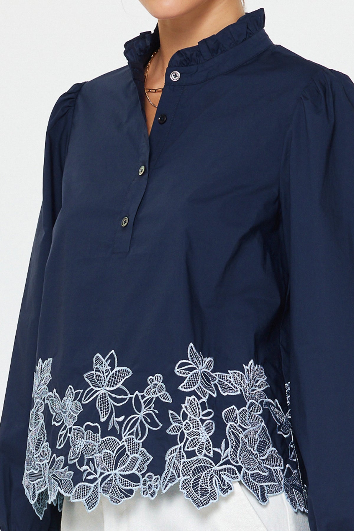 Lucy embroidered long sleeve blouse in cotton poplin with ruffle stand collar, puff sleeves, floral hem embroidery, and relaxed fit.