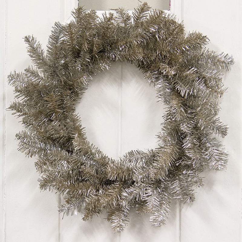 Glistening platinum pine wreath made of metallic plastic on a white paneled background.