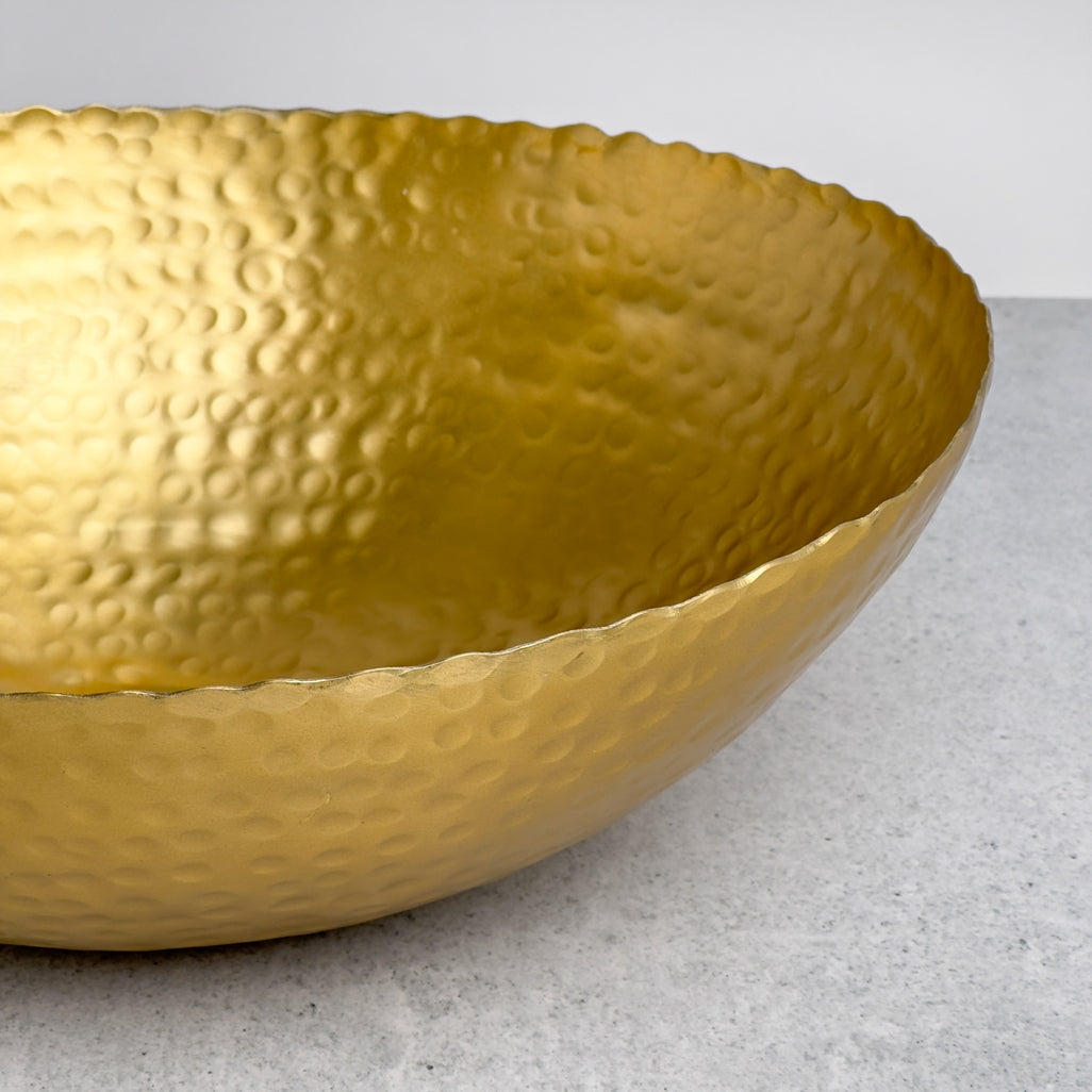 Close-up of a gold aluminum hammered oval bowl with a torn edge on a grey surface.