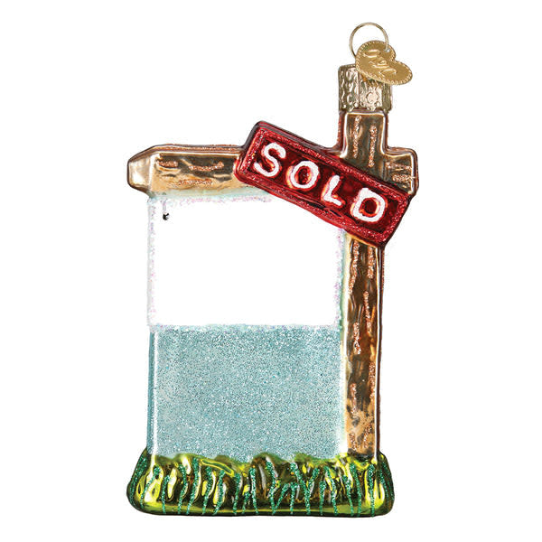 Glass ornament shaped like a real estate 'Sold' sign with hand-painted silver lettering and glitter finish.