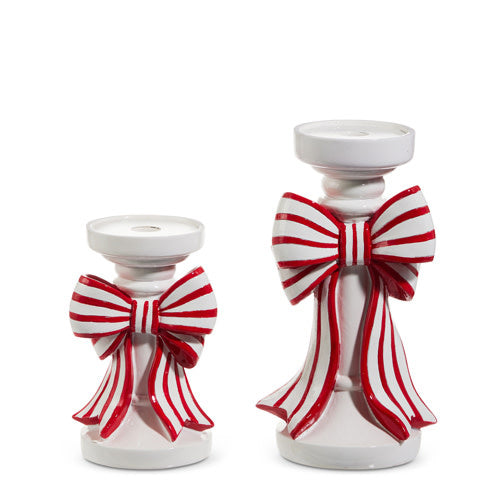 Red resin candle holder with white striped bow on iron base holding a taper candle