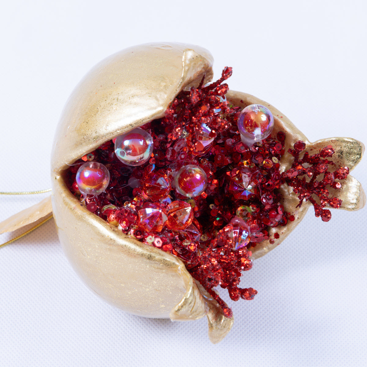 Gold pomegranate ornament with a split opening revealing red glitter and iridescent beads.
