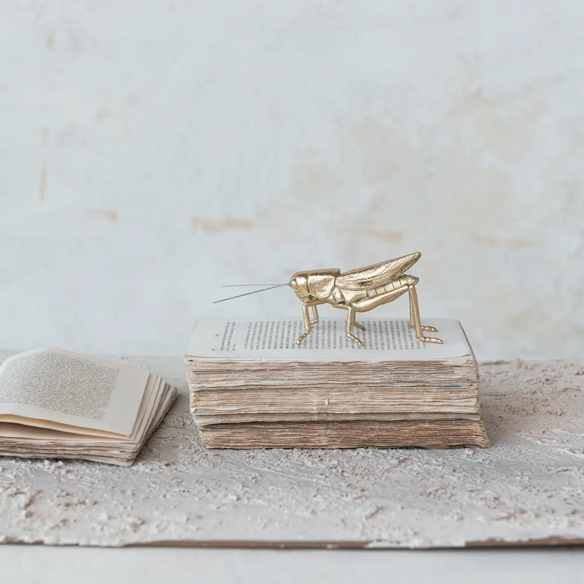 Golden resin grasshopper figurine with metal accents on a natural background