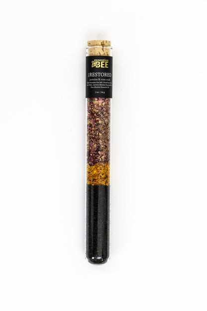 Glass vial containing mineral-rich sea salts with botanicals inside a mesh soaking pouch.
