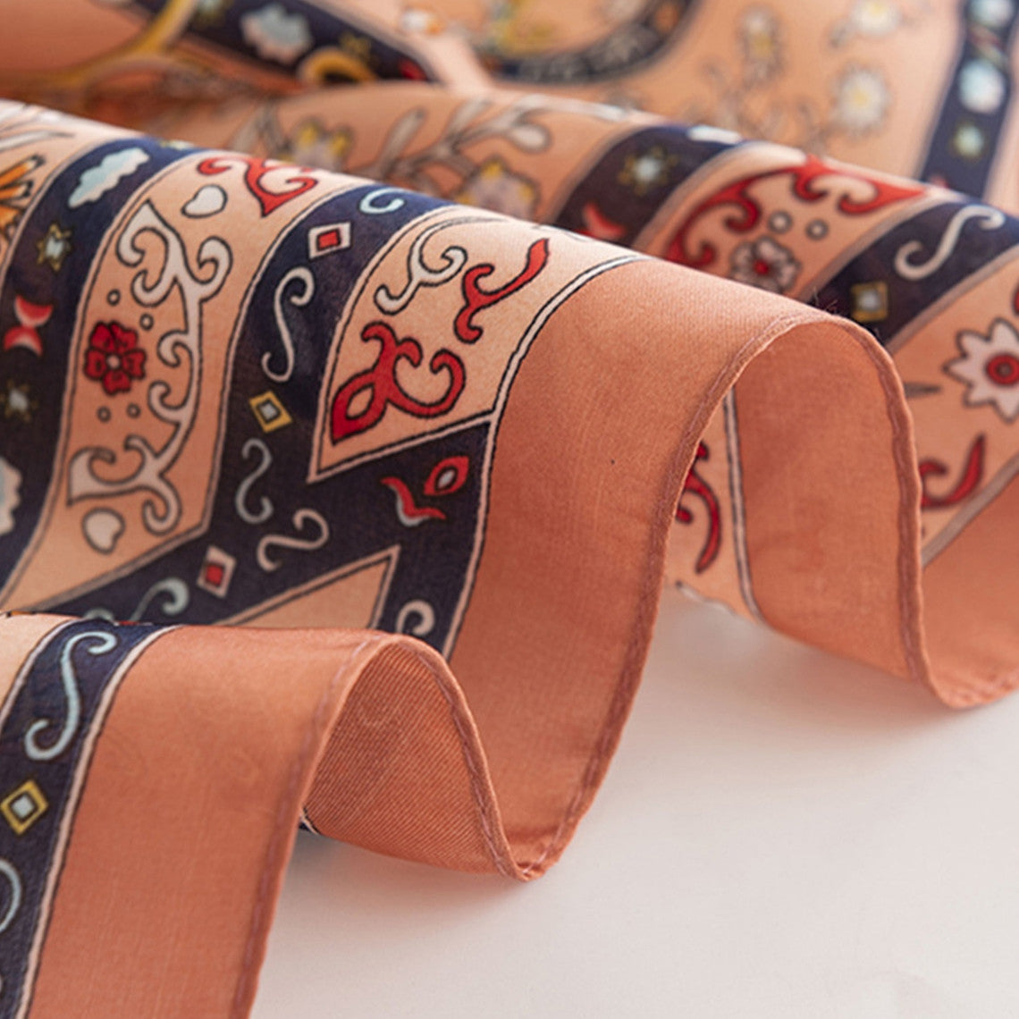 Close-up of a floral satin square scarf in peach with intricate red and blue patterns.