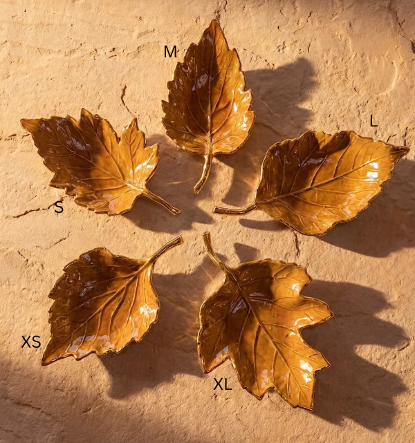 Five golden-brown, leaf-shaped enamel trays in various sizes arranged in a circle on a stone surface.