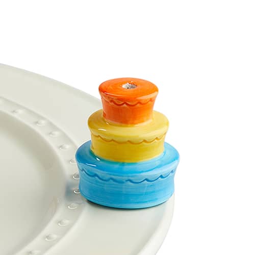 Three-tiered ceramic birthday cake mini attachment in orange, yellow, and blue on a white plate.