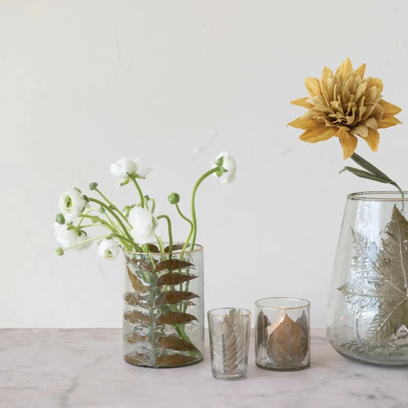 Hand-blown glass votive holder with embedded peepal leaves and a gold foil edge on a marble surface.