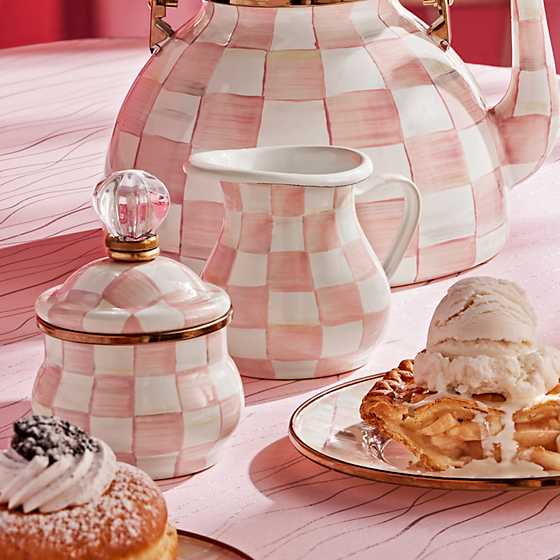Hand-painted pink and white checkered creamer on a table with matching tea set and desserts.