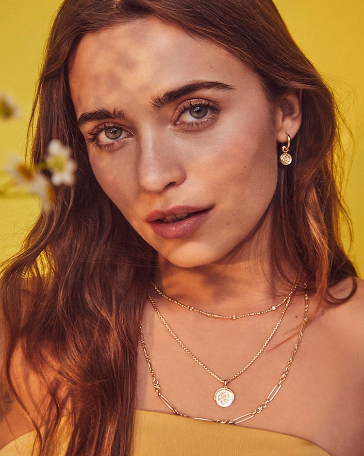 Woman wearing a gold Medallion Coin Triple Strand Necklace with three layered chains.