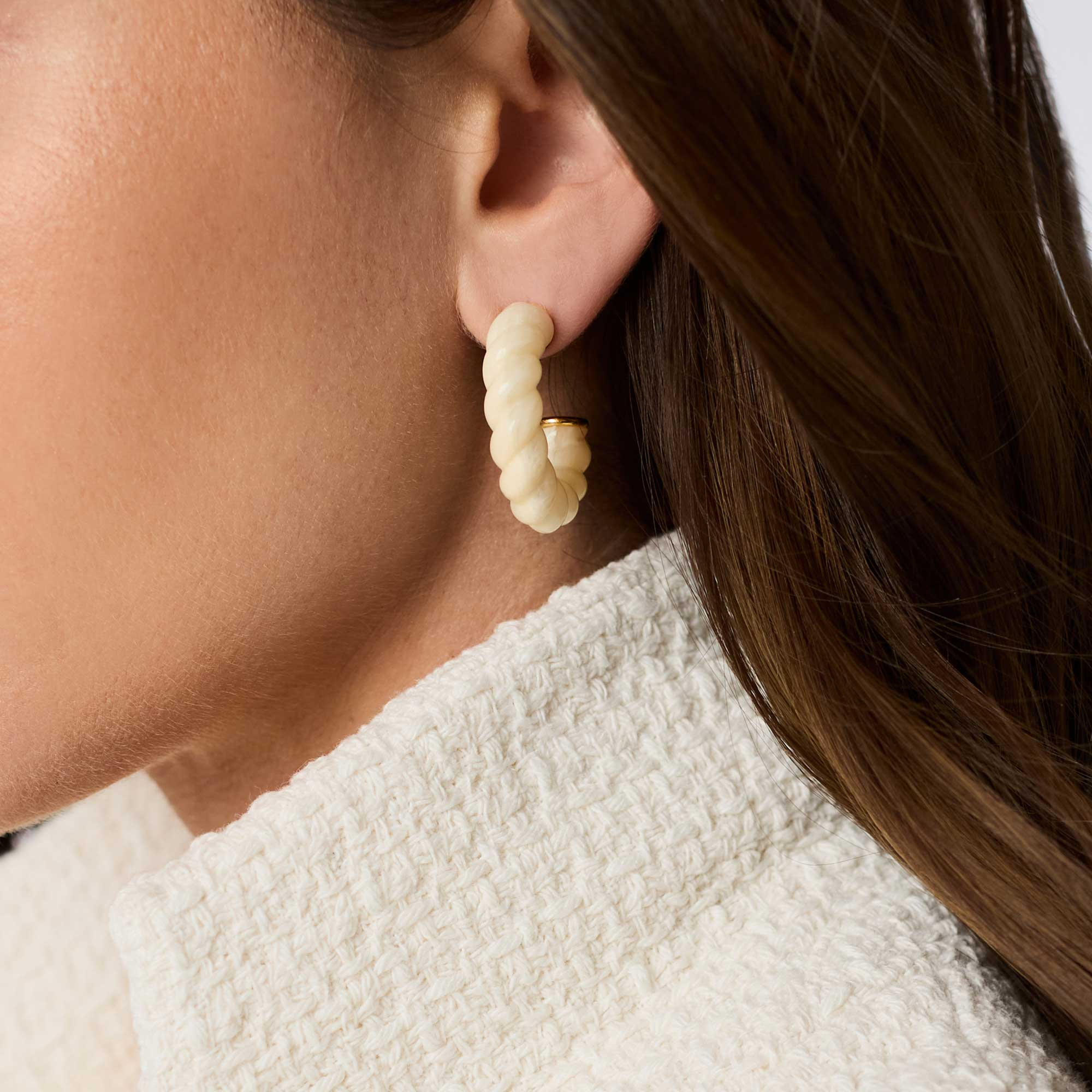A person wearing a cream-colored twisted resin Ravello Hoop earring with 24K gold plate accents.