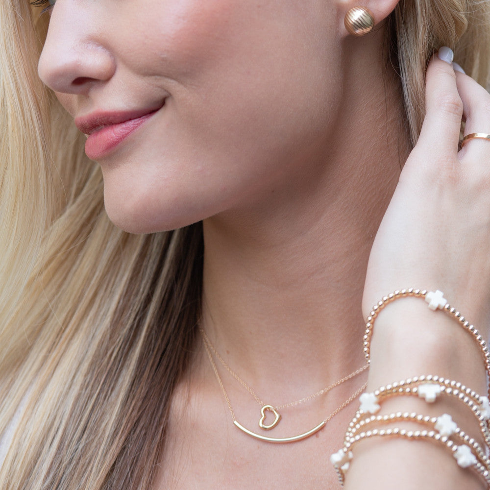 Woman wearing a 16-inch 14kt gold-filled Bliss Bar necklace layered with a heart pendant.