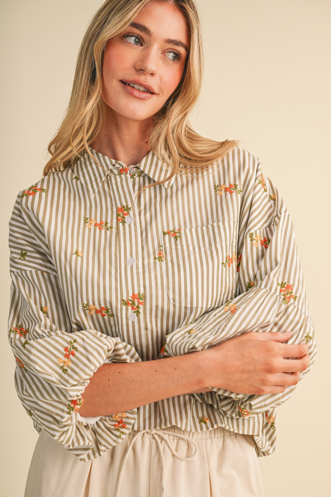 Woman wearing a striped floral embroidery button down top with bubble sleeves and a collar.