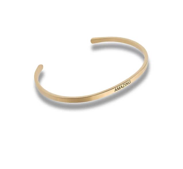 Gold-toned metal cuff bracelet with the word AMAZING engraved on the front.