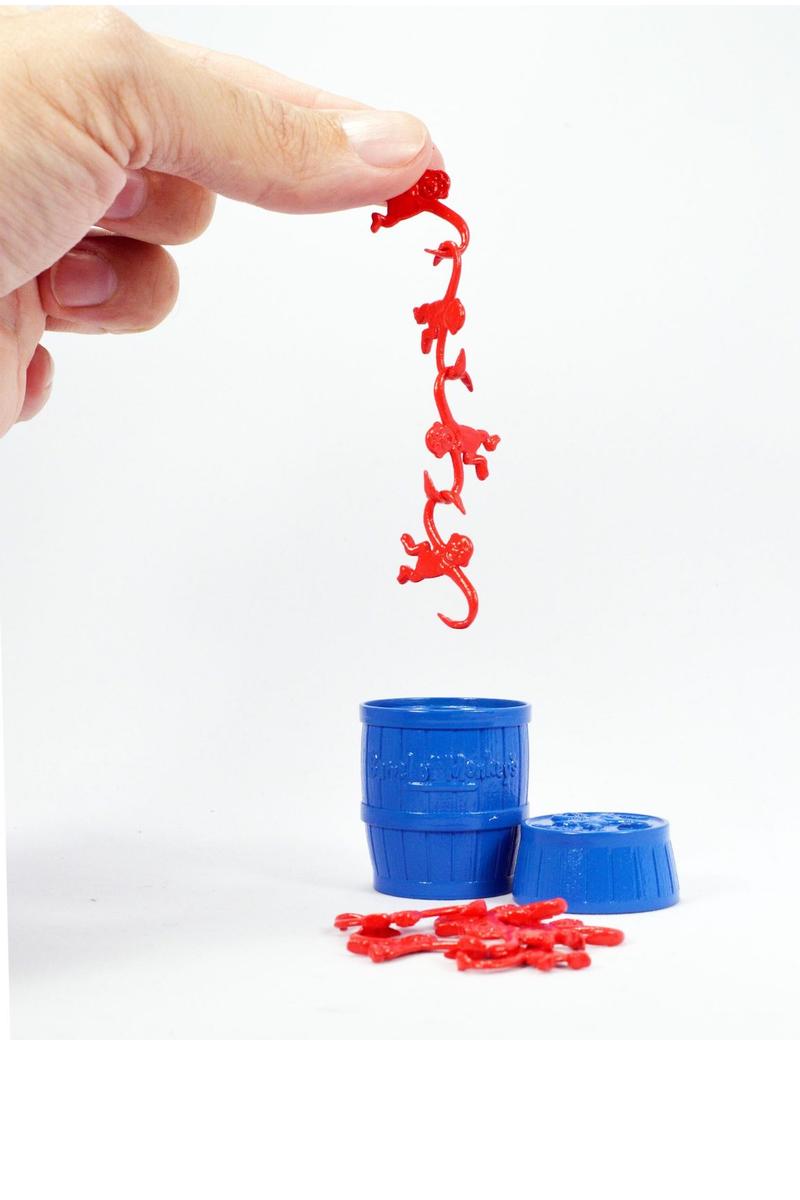 A hand holding a chain of four tiny red plastic monkeys over a small blue barrel.