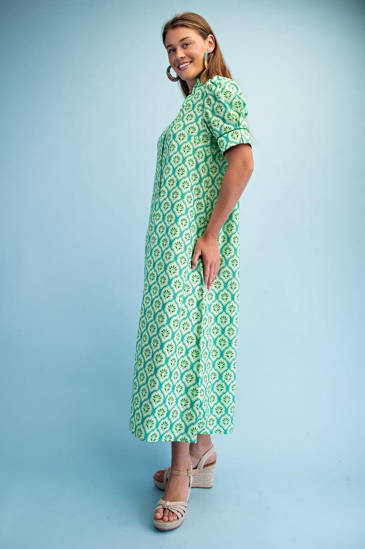 Woman in a green and white printed button-down midi dress with ruffled collar and short sleeves.