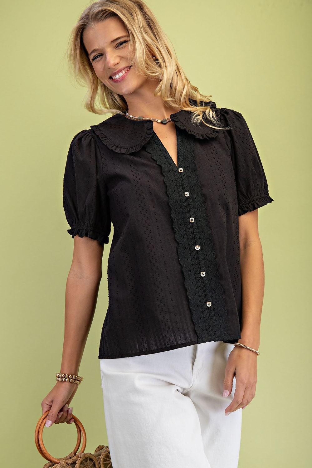Woman wearing a black Jane short puff sleeve blouse with a Peter Pan collar and white pants.