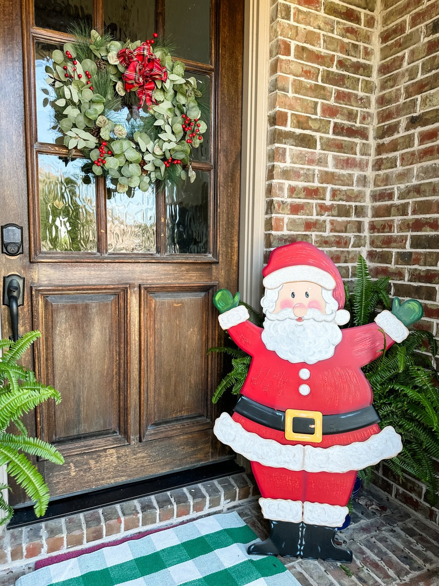 Large wooden Santa yard stake with a red suit, white beard, and green mittens by a front door.