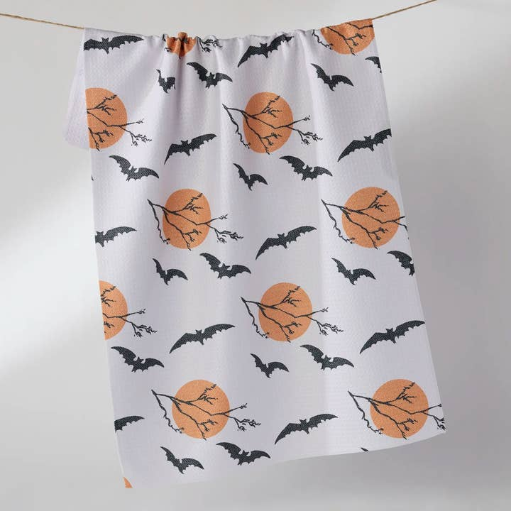 Halloween tea towel with a waffle weave featuring black bats and orange moons with tree branches.