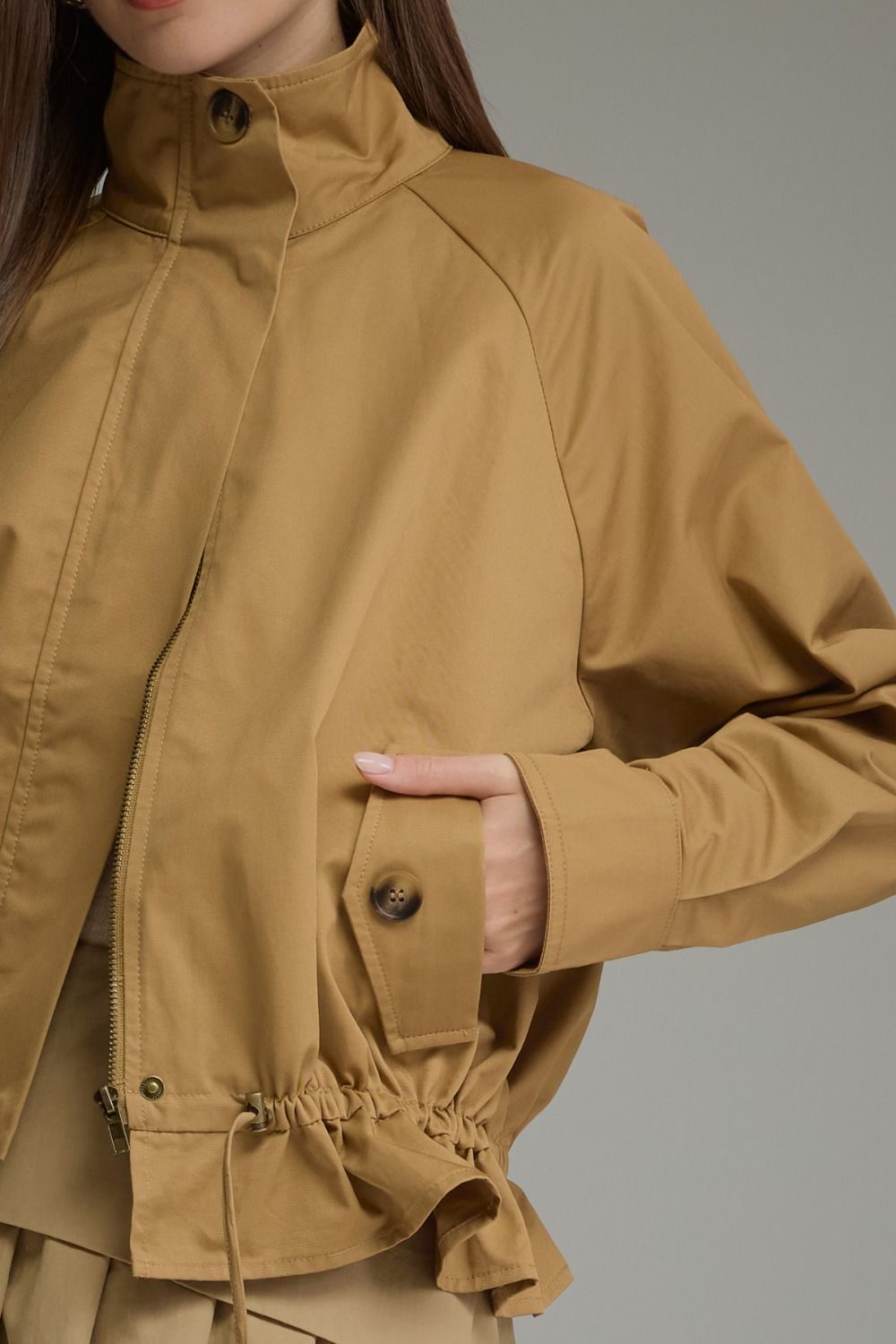 Close-up of the Andrea Solid Long Sleeve Jacket in tan, featuring a buttoned pocket and zip closure.