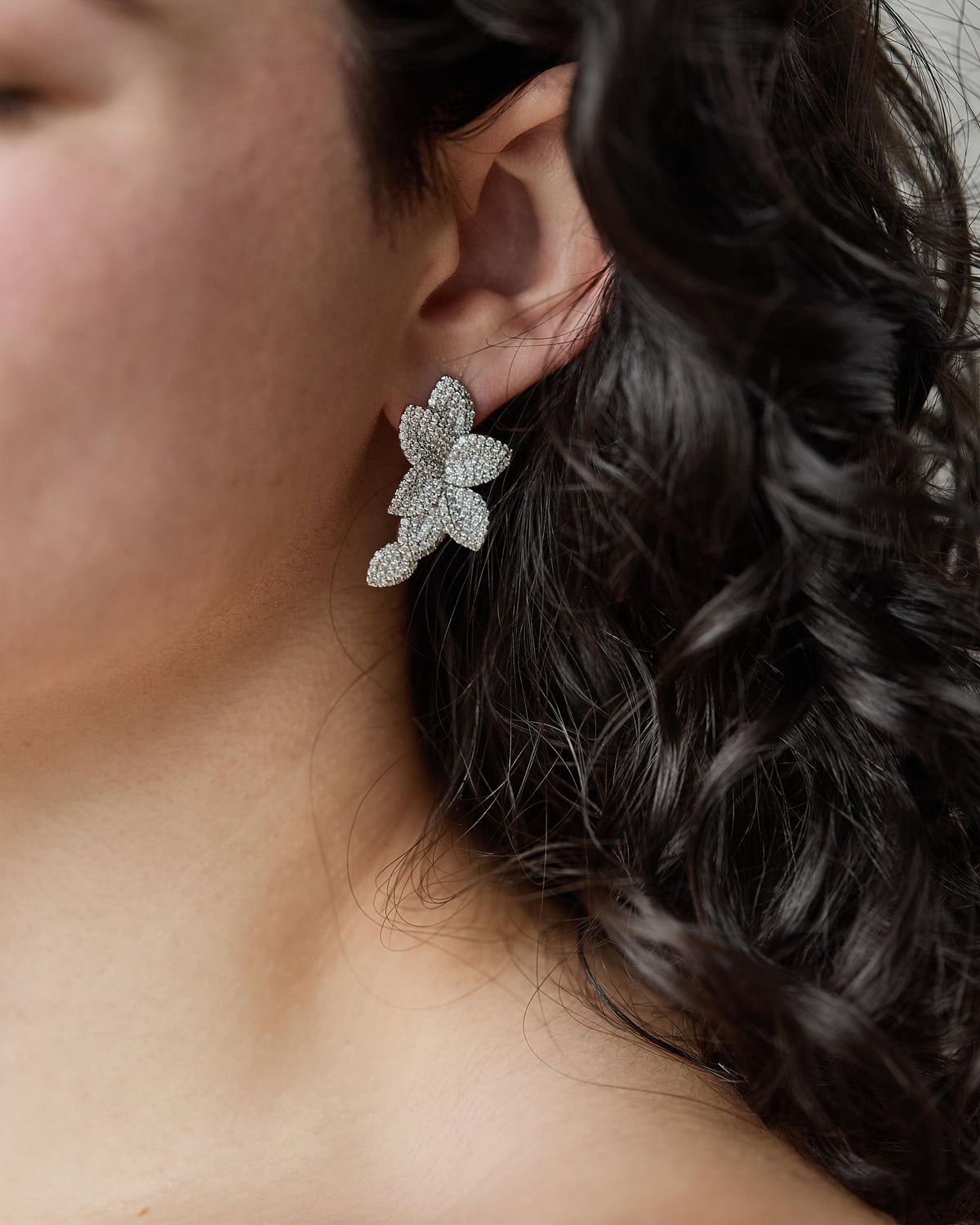 Close-up of a woman wearing a Mira Medium Plumeria Earring, a floral CZ stud with a drop design.
