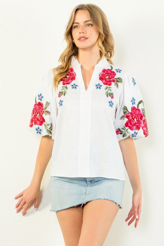 Woman wearing the Sofia WCT2896 white v-neck blouse with red floral embroidery and puff sleeves.
