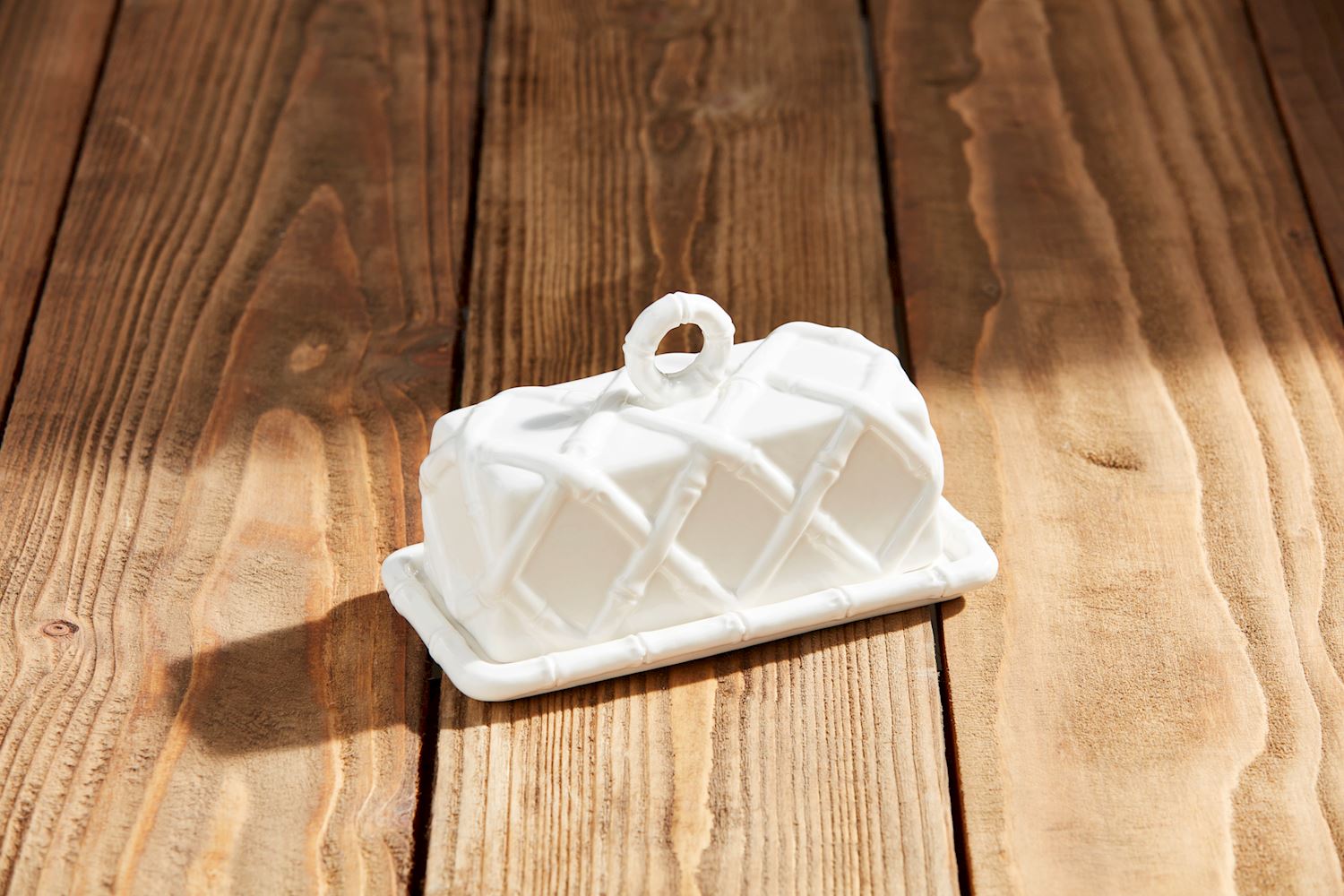 White stoneware butter dish with a raised bamboo lattice pattern on a wooden surface.