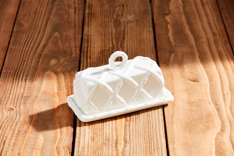 White stoneware butter dish with a raised bamboo lattice pattern on a wooden surface.