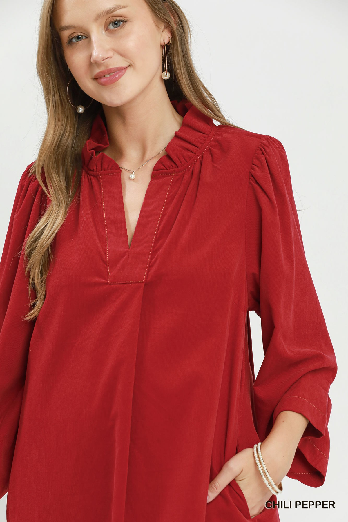 Close-up of a woman wearing a red corduroy split neck dress with puff sleeves and ruffle collar.